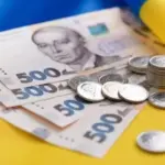 Жінка переглядає документи, на столі лежать гроші та ноутбук, що символізує судовий позов про повернення допомоги.