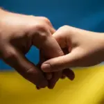 Символічне зображення рук, що тримаються, на фоні українського прапора, уособлюючи підтримку та надію для родин полонених.