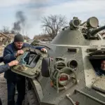 Поліція евакуює людей з Новорайської громади на Херсонщині, які сідають у броньований автомобіль, на фоні пошкоджених будівель