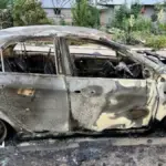 Згорілий автомобіль після атаки російського дрона у Херсоні, поруч медики надають допомогу постраждалим.