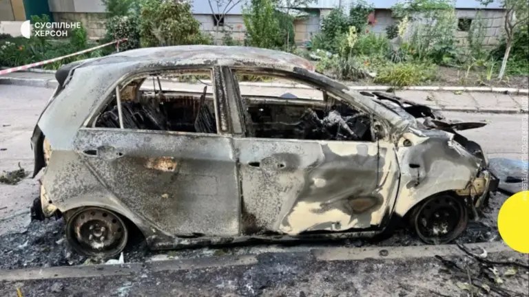 Згорілий автомобіль після атаки російського дрона у Херсоні, поруч медики надають допомогу постраждалим.