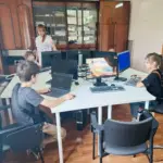 Група людей вивчає комп'ютерну грамотність у класі, жінка-викладачка допомагає