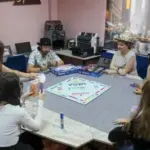 Херсонські підлітки грають у "Монополію" в центрі "Вікно в Америку", обговорюючи стратегії та історію гри.