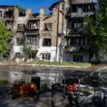 Зруйновані будинки та пошкоджена інфраструктура в Херсоні після російських атак, на фоні дим.