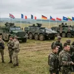 Військові НАТО з бронетехнікою на навчаннях на тлі прапорів країн Альянсу