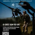 Український військовий стоїть на позиції в повній амуніції, на фоні прапора України.
