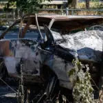 Пошкоджений автомобіль після удару російського дрона в Херсоні, поруч працюють правоохоронці