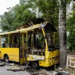 Пошкоджений автобус після обстрілу у Херсоні, на фоні розбиті будівлі, день