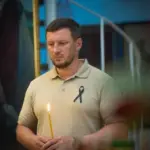 Український солдат стоїть на колінах перед меморіалом, присвяченим загиблим у російському полоні, з квітами.