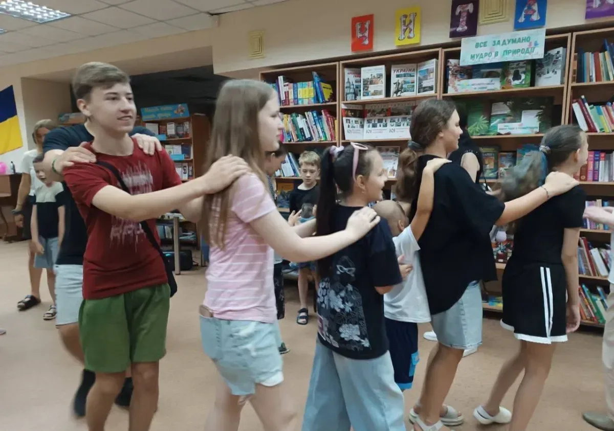 Волонтери з різних країн грають з дітьми та дарують їм подарунки у херсонській бібліотеці, створюючи радісну атмосферу. 1